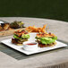 A Front of the House white porcelain square plate with sandwiches, lettuce, bacon, and fries.