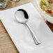 An Acopa Ridge stainless steel bouillon spoon on a napkin next to a bowl of soup.