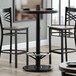 A Lancaster Table & Seating cast iron bar height table base with a black finish and a metal foot rest.
