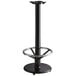 A Lancaster Table & Seating cast iron bar height table base with a metal foot rest.