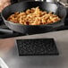 A black Lodge silicone trivet with a skillet pattern holding a black pan of food.