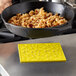 A person using a yellow Lodge silicone trivet with a skillet to cook food on a table.