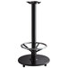 A Lancaster Table & Seating cast iron bar height table base with a foot rest and table equalizers with a black metal bar stool.