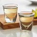 Two Anchor Hocking shot glasses filled with brown liquid on a wooden board.