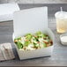 A salad in a Fold-Pak white paper take-out box.
