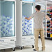 An Avantco indoor ice merchandiser with a man reaching for a stack of plastic bags.