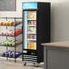 An Avantco black glass door merchandiser freezer with a variety of products on shelves.