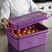 A woman in a chef's uniform holding a Vollrath purple food storage container full of apples.