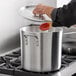 A person using a spoon to cook in a Choice 20 qt. aluminum stock pot.