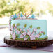 A cake with blue flowers and birds on top made using a Wilton Nature Designs silicone mold on a table in a bakery display.