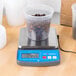 An AvaWeigh compact digital portion control scale with a plastic container of coffee beans on it.