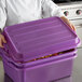 A woman in a chef's uniform holding a purple Vollrath Traex food storage container lid.