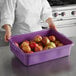A woman in a chef's uniform holding a Vollrath purple plastic food storage container full of red apples.
