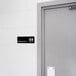 A grey door with a Thunder Group black and white unisex restroom sign on it.