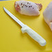 A Dexter-Russell Sani-Safe knife set on a cutting board with a chef's knife cutting a raw chicken breast.