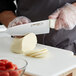 A person cutting a piece of cheese on a cutting board with a Dexter-Russell knife.
