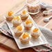 A white plate with small Wilton mini tarts topped with oranges and coconut chips.
