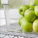 A Cambro clear food storage container with a sliding lid and a tray of green apples inside.