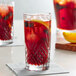 A highball glass with a red drink, ice, and fruit on a table.