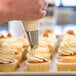 A person using Rich's Bettercreme Cream Cheese Whipped Icing to frost a cupcake.