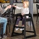 A little girl sitting in a Lancaster Table & Seating wooden high chair with a black finish.