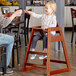 A little girl sitting in a Lancaster Table & Seating wooden high chair at a table.