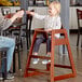 A little girl sitting in a Lancaster Table & Seating wooden high chair.