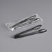 Two Visions black plastic tongs with handles sitting on a counter.