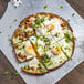 A Rich's gluten-free cauliflower pizza crust topped with eggs, bacon, and green onions on a metal tray.