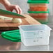 A hand using a knife to cut food in a Cambro food storage container on a cutting board.
