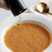 A hand pouring Regal Gourmet Peppercorn Medley into a bowl of soup.