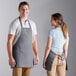 A man and woman wearing Choice grey front of house aprons in a professional kitchen.