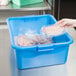 A hand putting a plastic bag of raw meat in a blue Vollrath food storage container.