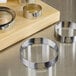 A stack of Fat Daddio's stainless steel round tart rings on a wooden surface.