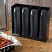 A black San Jamar countertop organizer with plastic portion cups and lids.