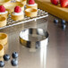 A silver stainless steel round tartlet ring on a table with small tartlets and fruit.