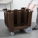 A person pushing a brown Cambro dish caddy with wheels.