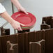 A person holding a stack of plates in a brown Cambro dish caddy with a black circle.