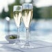 Two Arcoroc SAN plastic champagne flutes filled with champagne on a table.