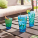 Arcoroc blue plastic cooler glasses filled with blue drinks and cucumber slices on a table.