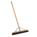 A Carlisle commercial push broom with a wooden handle.