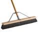A Carlisle commercial push broom with a wooden handle and black bristles.