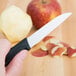 A person's hand uses a Victorinox Sheep's Foot Paring Knife with a black handle to peel an apple.