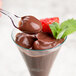 A clear WNA Comet tasting spoon full of chocolate pudding with strawberries.