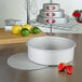 A Fat Daddio's round white cheesecake pan with a red removable bottom on a counter with strawberries and limes.