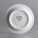 A white porcelain saucer with black text reading "Corona"
