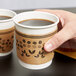 A hand placing a Choice coffee cup sleeve on a coffee cup.