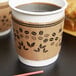 A brown paper coffee cup with a Choice coffee cup sleeve filled with coffee on a table.