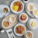 A table set with Acopa Foundations white narrow rim melamine plates, bowls, and cups of food.