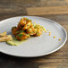A Corona by GET Enterprises Cosmos porcelain coupe plate with shrimp and corn on a wood table.